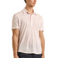 A man wearing a tailored fit light pink Sebastian Linen Polo by Orlebar Brown and dark pants, standing against a plain background.