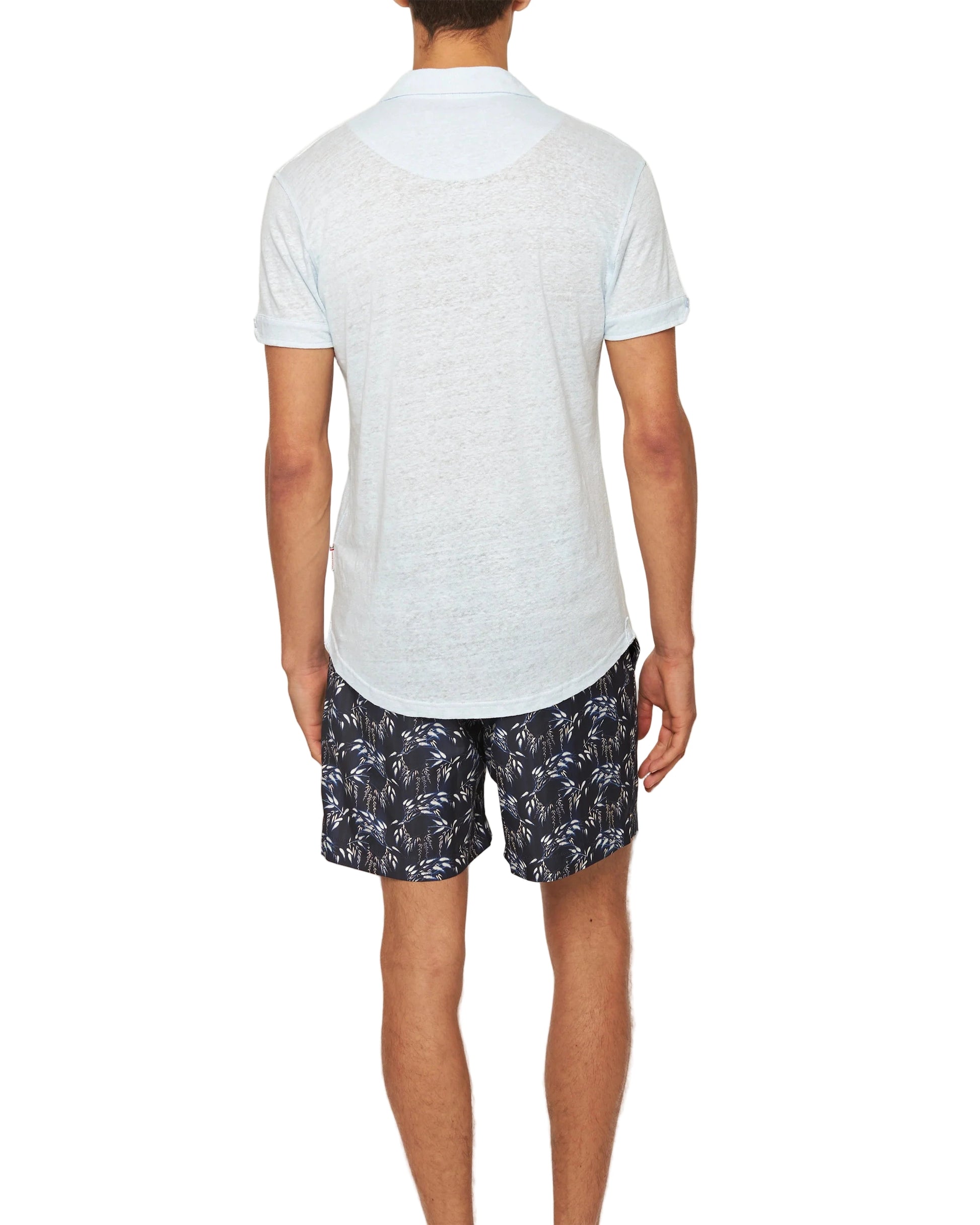 A man stands facing away, wearing the Sebastian Linen Polo by Orlebar Brown and dark shorts with a white leaf pattern, set against a plain white background.