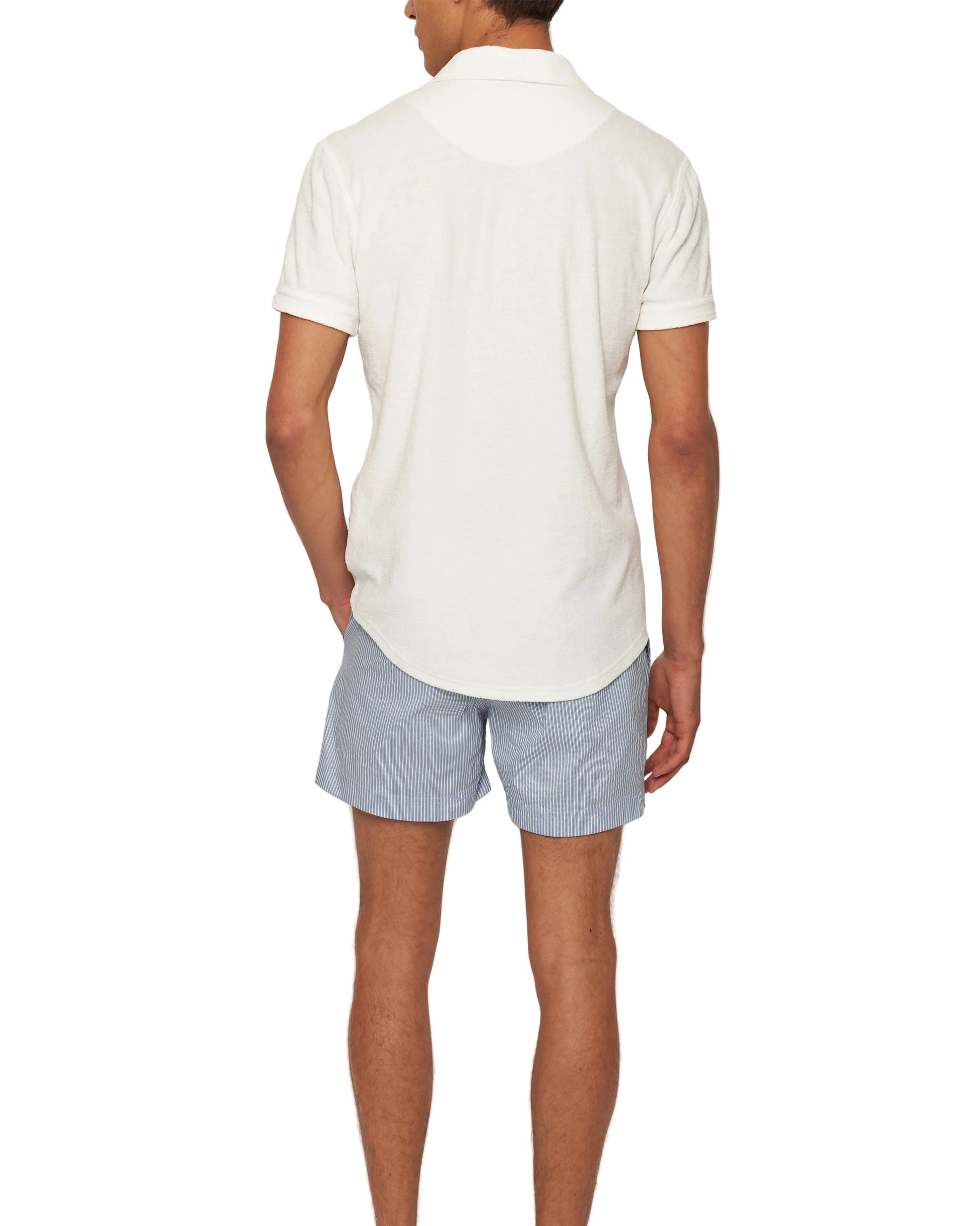 A man faces away, wearing the Orlebar Brown Terry Polo in white, crafted from breathable cotton towelling, paired with light blue striped shorts against a plain white background.