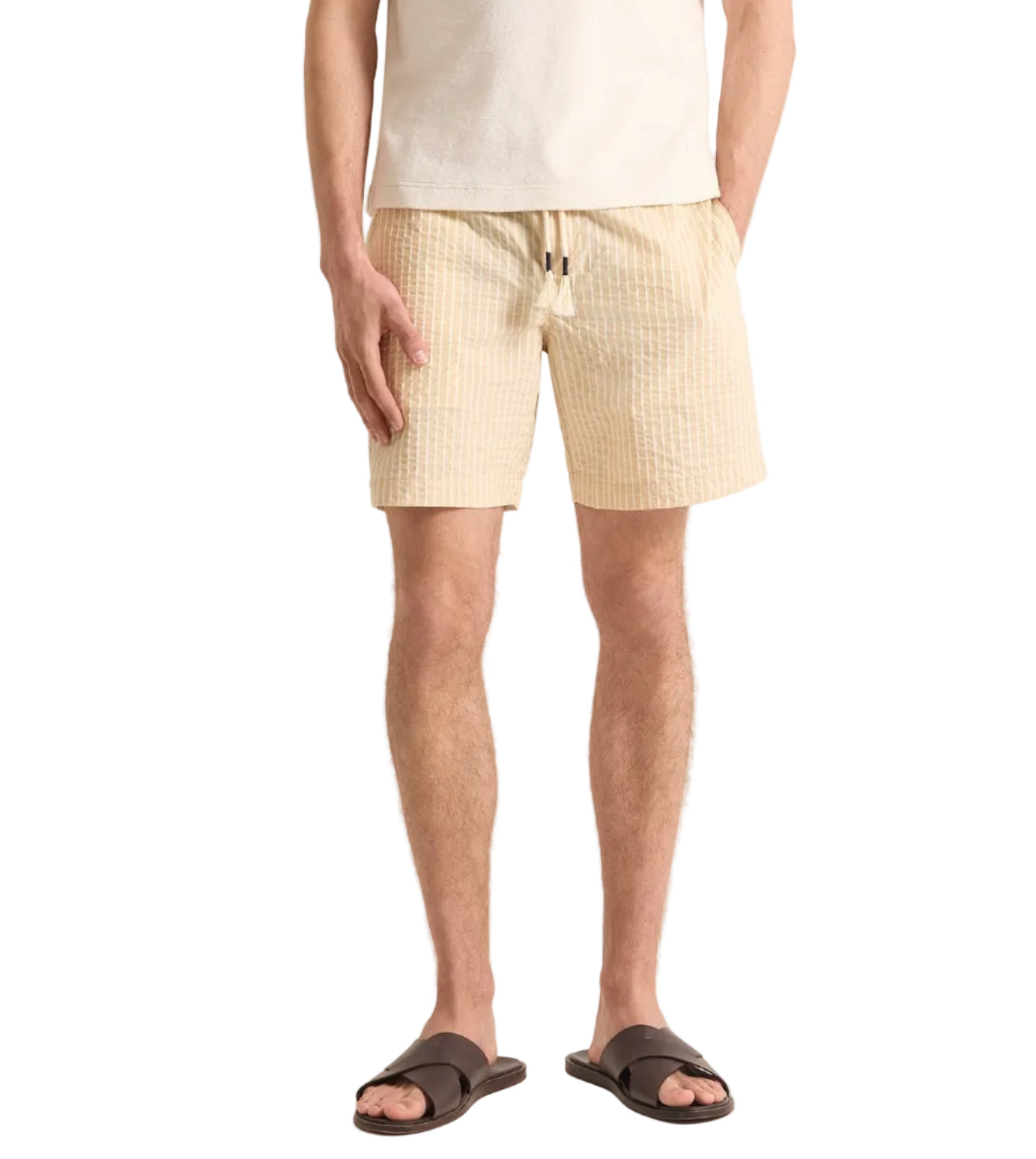 A person wears the Orlebar Brown Sonoran Short Seersucker Stripe with an elasticated waistband, a cream t-shirt, and brown sandals, standing against a plain background.