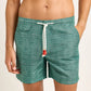 A person is wearing Orlebar Brown’s Standard Riptide Woven Swim Shorts in green print with a white drawstring, shown from waist to mid-thigh with hands in the pockets.