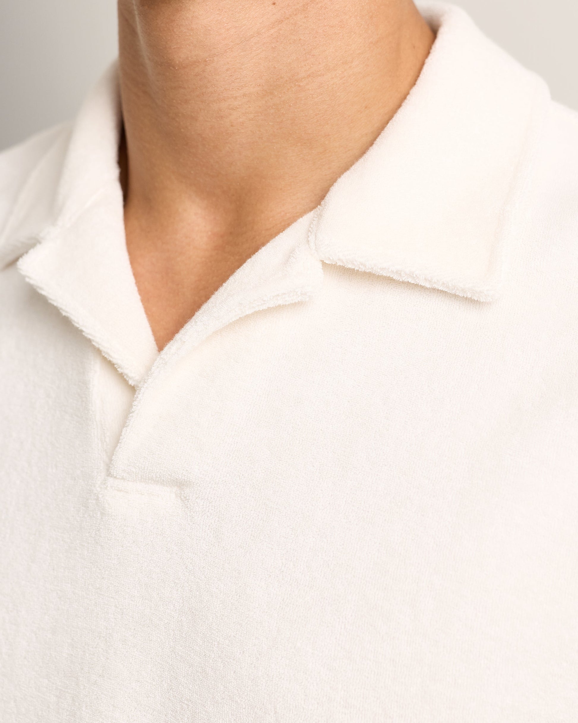 Close-up of a person wearing the Orlebar Brown Terry Resort Polo, showcasing its soft, textured white fabric. Only the neck and upper chest are visible.