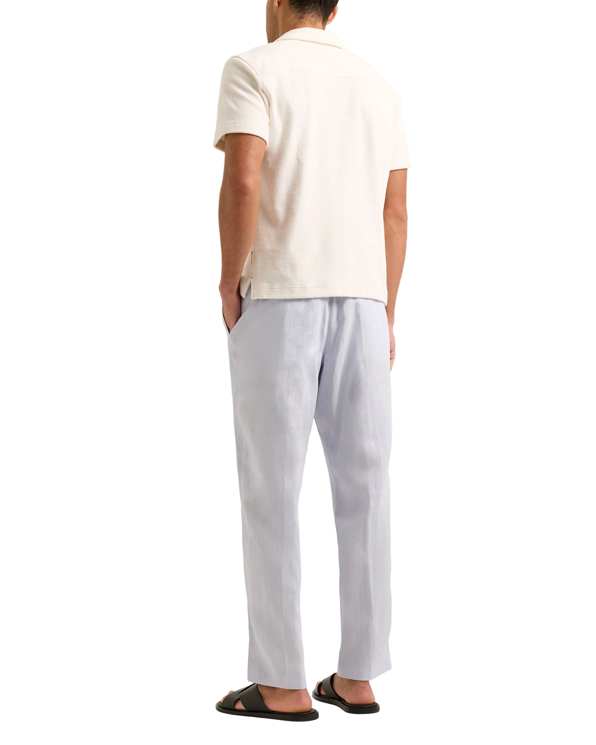 A man faces away, wearing the Orlebar Brown Terry Resort Polo with short sleeves and a Capri collar, paired with light blue pants and black sandals, all set against a plain white background.