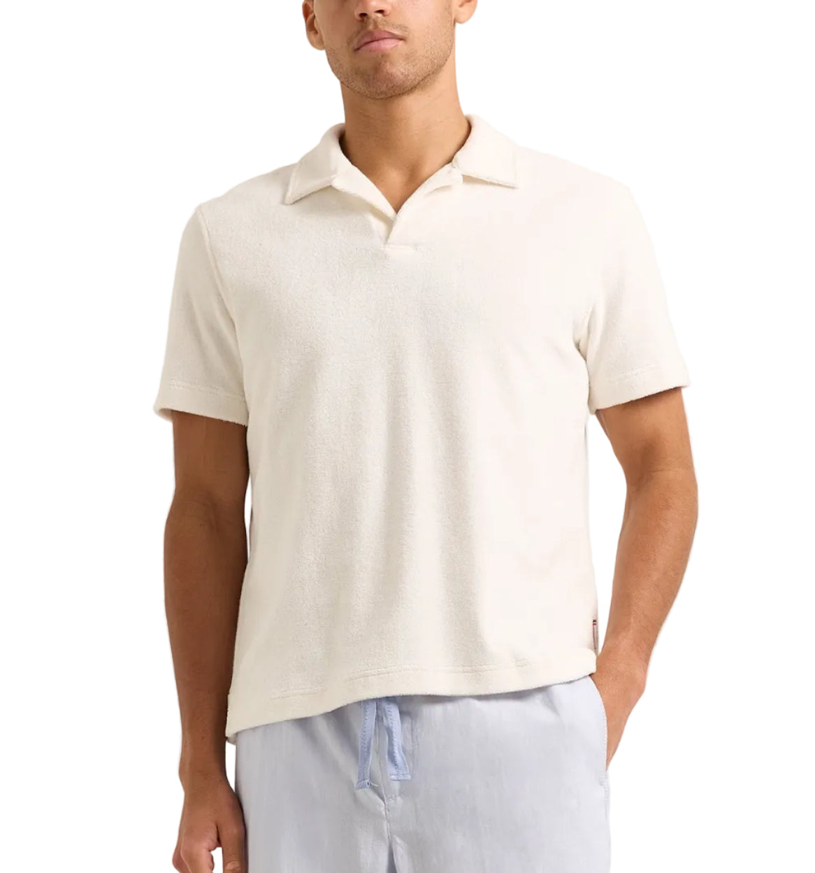 A man wears the Orlebar Brown Terry Resort Polo, a short-sleeve off-white organic cotton towelling shirt, with light blue drawstring pants, standing against a plain background.