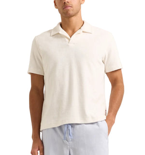 A man wears the Orlebar Brown Terry Resort Polo, a short-sleeve off-white organic cotton towelling shirt, with light blue drawstring pants, standing against a plain background.