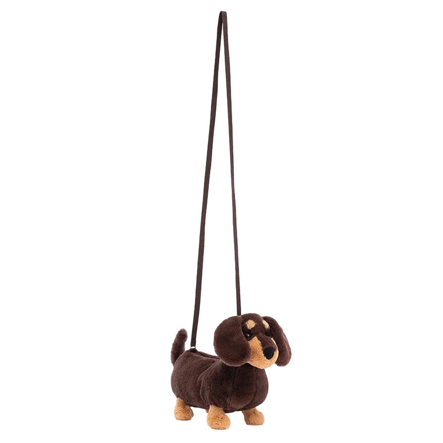 The Jellycat Otto Sausage Dog Shoulder Bag is a plush brown and tan dachshund-shaped purse with a long strap, making it a charming accessory for city strolls.