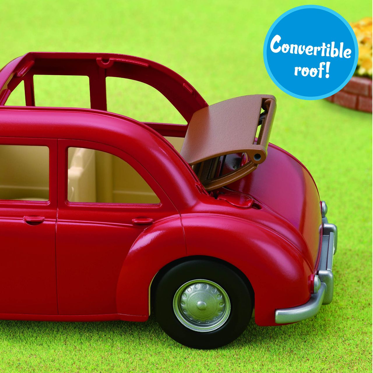 A red Calico Critters Family Cruising Car with a folding convertible roof is pictured on green grass, illustrating the roof as it moves back. The playful vehicle is an ideal addition to any Calico Village scene. A blue circle in the corner highlights, “Convertible roof!”.