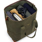 The Bennett Winch Medium Cargo by Bennett Winch is an open green tote bag made from waterproof nylon, containing a rolled-up navy sweater, a camera, gray fabric, a beige item, and a stainless steel bottle.