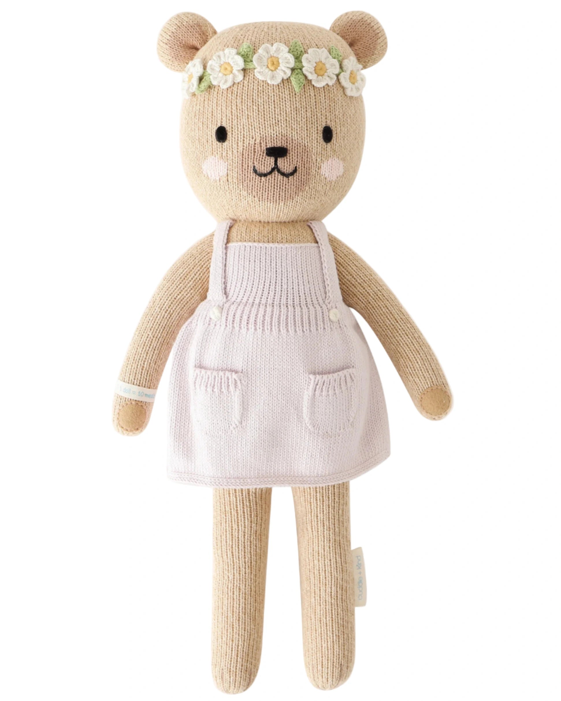 Olivia the Honey Bear by Cuddle + Kind is a 20" knitted teddy bear doll dressed in a white apron and a floral headband, ready to inspire imagination in any playroom.