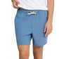 A person wearing a white shirt and blue Onia Land to Water Short 6" with four-way stretch stands, one hand slightly lifting the shirt, the other resting by their side.