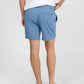 A person stands barefoot, shown from the back, wearing a white shirt and light blue Onia Land to Water Short 6" featuring an elastic waistband, four-way stretch fabric, and a single back pocket.