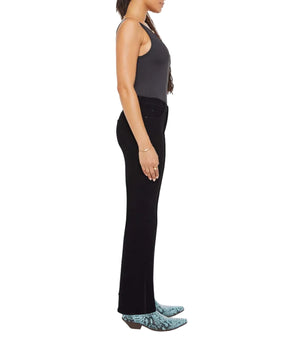 A woman stands in profile against a white background, wearing Mother Lil Kick It black sleeveless top and pants, paired with blue snake-print cowboy boots.