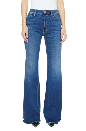 A person wearing Mother PETITES The Lil Doozy Fray high-rise blue flare jeans with a white top, standing relaxed. The jeans have stretch denim for comfort, a slight fade, and visible seams.