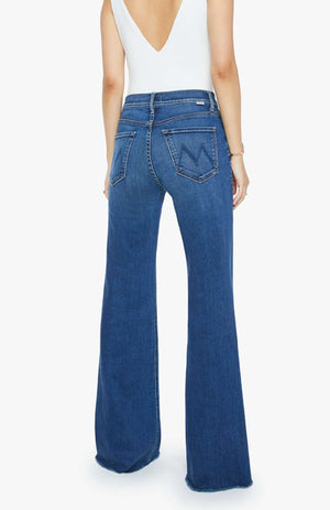 A woman is seen from behind wearing Mother PETITES The Lil Doozy Fray jeans—blue, high-rise, stretch denim with a flared leg—and a white sleeveless top featuring a deep V-cut back.