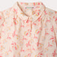 The Girls’ Mathilda Blouse by Bonpoint is a light pink collared blouse for girls, featuring a red and yellow floral print, a button-down front, and text such as “Bonpoint,” “PARIS,” and “1975” printed across the organic cotton fabric.