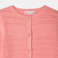 Close-up of the Bonpoint Girls’ Mia Cardigan, a pink button-front style featuring a round neckline and patterned knit with a repeating design of small decorative musical notes, eyelet details, and raised cherries.