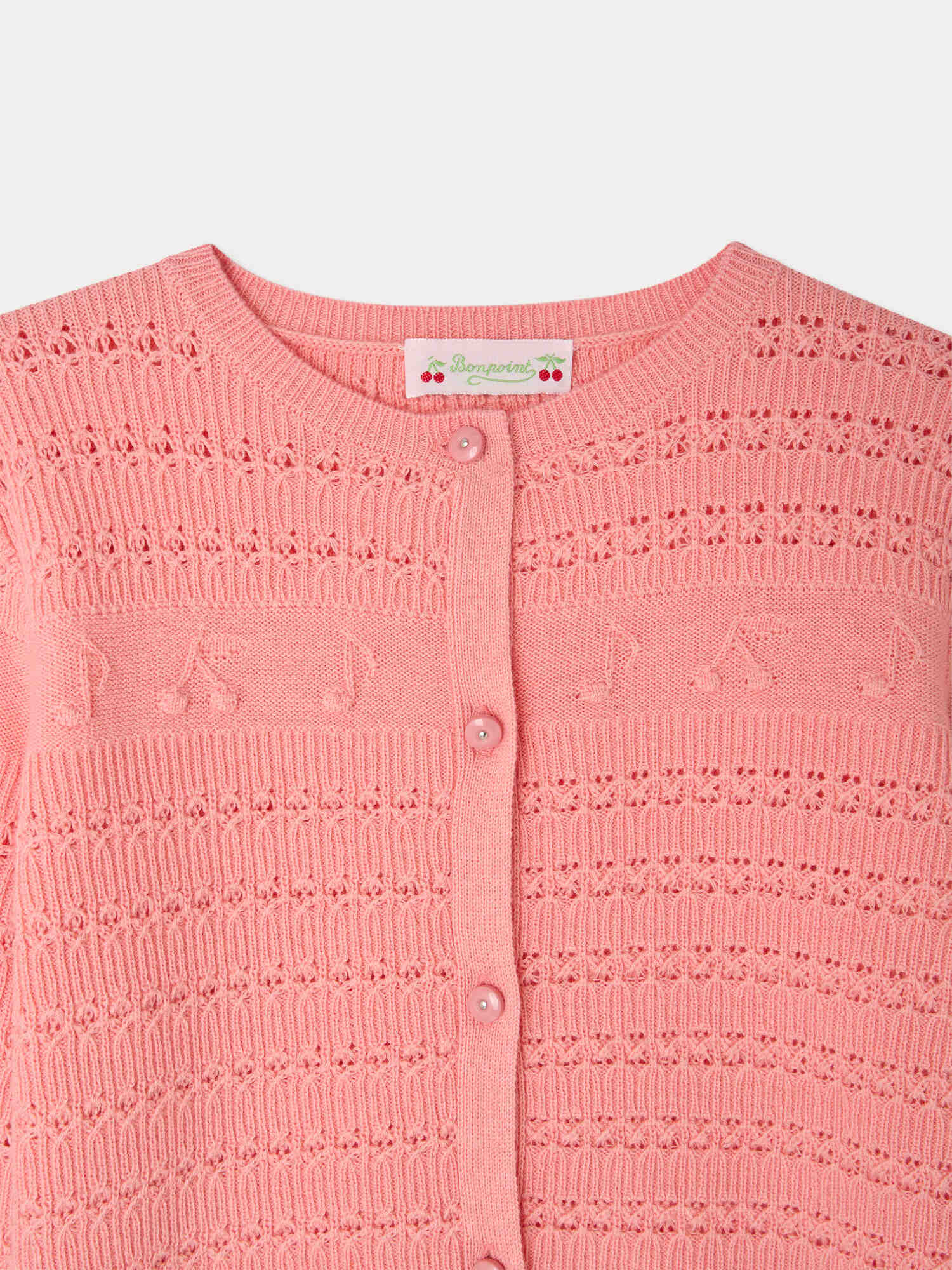 Close-up of the Bonpoint Girls’ Mia Cardigan, a pink button-front style featuring a round neckline and patterned knit with a repeating design of small decorative musical notes, eyelet details, and raised cherries.