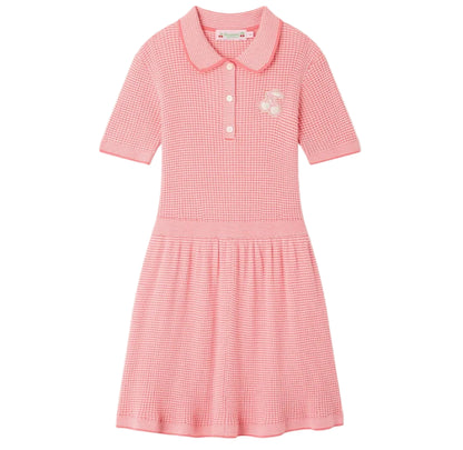The Girls’ Marlie Dress by Bonpoint is a pink short-sleeve knit dress for girls, featuring a collar, three front buttons, a subtle gingham print, and a small cherry embroidery on the chest.