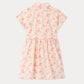 The Girls’ Gisele Dress by Bonpoint is a light pink shirt dress featuring short sleeves, a collar, and a button-down top with a belted waist. Made from organic cotton, it showcases an all-over tropical floral print with palm trees and “1975” in muted pink and orange tones.