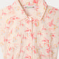 Close-up of the Girls’ Gisele Dress by Bonpoint in light beige organic cotton, featuring a pink floral and fruit print, white buttons, two front pockets, and scattered “1975” and “Paris” text on the fabric.