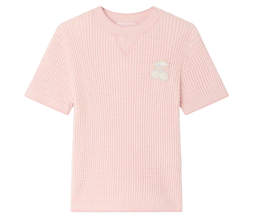 The Girls’ Melie Sweater by Bonpoint is a light pink, short-sleeve waffle knit shirt featuring a waﬄed texture and a white cherry patch on the left chest, shown against a plain white background. Ideal for those wanting the cozy comfort of an organic cotton sweater in a playful girls’ style.