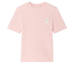 The Girls’ Melie Sweater by Bonpoint is a light pink, short-sleeve waffle knit shirt featuring a waﬄed texture and a white cherry patch on the left chest, shown against a plain white background. Ideal for those wanting the cozy comfort of an organic cotton sweater in a playful girls’ style.
