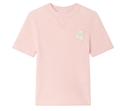 The Girls’ Melie Sweater by Bonpoint is a light pink, short-sleeve waffle knit shirt featuring a waﬄed texture and a white cherry patch on the left chest, shown against a plain white background. Ideal for those wanting the cozy comfort of an organic cotton sweater in a playful girls’ style.