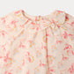 Close-up of the Bonpoint Baby Girls’ Dolci Blouse in light pink organic cotton, featuring a ruffled collar and cherry illustrations alongside “Bonpoint,” “1975,” and “Paris” text in soft pink and orange tones, elegantly finished with a delicate floral print.