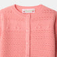 Close-up of the Bonpoint Baby Girls’ Mahana Cardigan in pink, showcasing its round neckline, button-front closure, and delicate decorative knit details with small music note patterns on the chest.