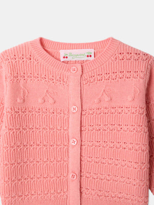 Close-up of the Bonpoint Baby Girls’ Mahana Cardigan in pink, showcasing its round neckline, button-front closure, and delicate decorative knit details with small music note patterns on the chest.