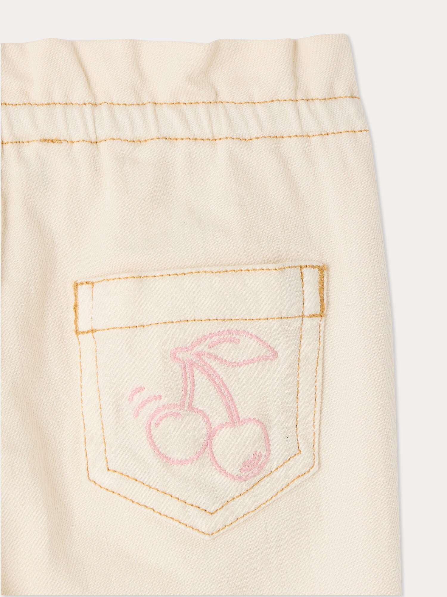 Close-up of a cream-colored, cotton-rich pocket with orange stitching and a pink outline drawing of two cherries, featured on the Bonpoint Baby Girls’ Luciole Pant—perfect for adding a charming embroidered accent to organic babywear.