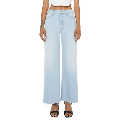 Model wears the Mother Petites Lil Hustler Roller Fray high-waisted, light-wash wide leg jeans with raw hems—ideal for petite denim options—styled with black heeled sandals and a white crop top; shown from the waist down against a white background.