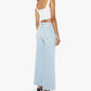 A woman stands with her back to the camera, wearing the Mother Petites Lil Hustler Roller Fray high-rise jeans in light blue, paired with a white sleeveless crop top and black heeled sandals, set against a plain white background.