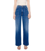 A person is wearing the Mother Petites Lil Patch Maven Sneak—high-waisted, wide-leg blue jeans made from recycled stretch denim with front patch pockets—paired with a white sleeveless top and sandals, standing against a white background.
