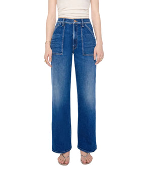 A person is wearing the Mother Petites Lil Patch Maven Sneak—high-waisted, wide-leg blue jeans made from recycled stretch denim with front patch pockets—paired with a white sleeveless top and sandals, standing against a white background.