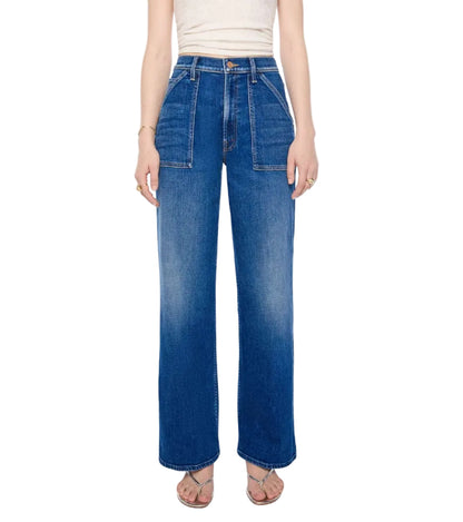 A person is wearing the Mother Petites Lil Patch Maven Sneak—high-waisted, wide-leg blue jeans made from recycled stretch denim with front patch pockets—paired with a white sleeveless top and sandals, standing against a white background.