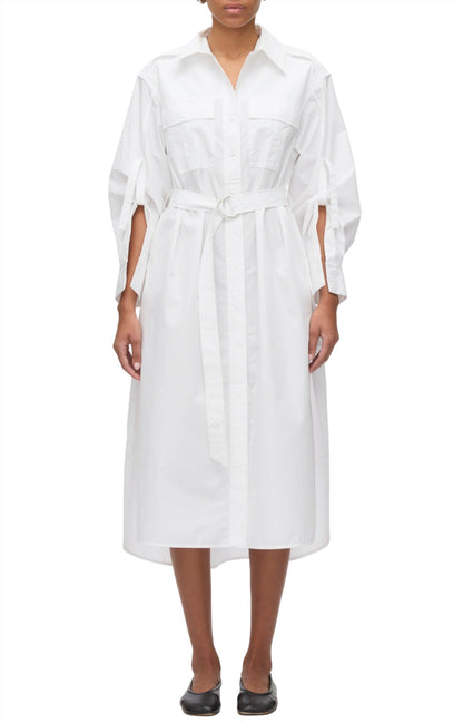 A person wearing the 3.1 Phillip Lim Poplin Utility Midi Shirt Dress in white, crafted from technical poplin and featuring a tied belt. It is styled with black flats for a sleek look.