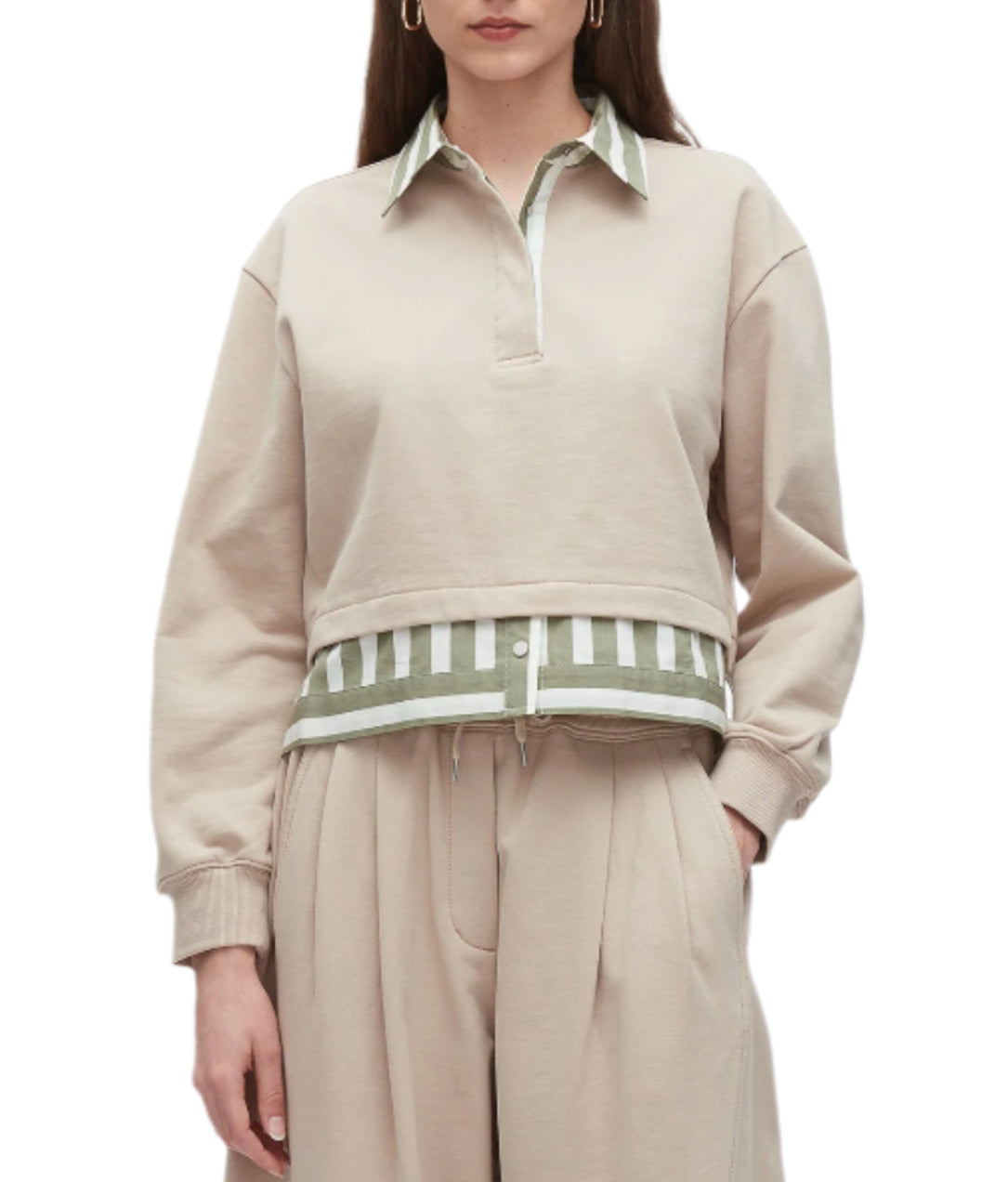 A woman wears the 3.1 Phillip Lim Cropped Polo with Stripe Combo Top, featuring a beige collared sweatshirt layered over a green and white striped shirt, paired with beige pleated pants.