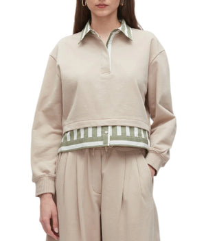 A woman wears the 3.1 Phillip Lim Cropped Polo with Stripe Combo Top, featuring a beige collared sweatshirt layered over a green and white striped shirt, paired with beige pleated pants.