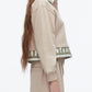A woman stands in profile wearing the 3.1 Phillip Lim Cropped Polo with Stripe Combo Top—a beige long-sleeve layer with a green-and-white striped polo detail underneath, perfect for effortless layering.
