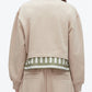 A person is seen from the back wearing the 3.1 Phillip Lim Cropped Polo with Stripe Combo Top, a beige jacket featuring green and white striped silk-cotton trim at the hem, paired with beige pants.