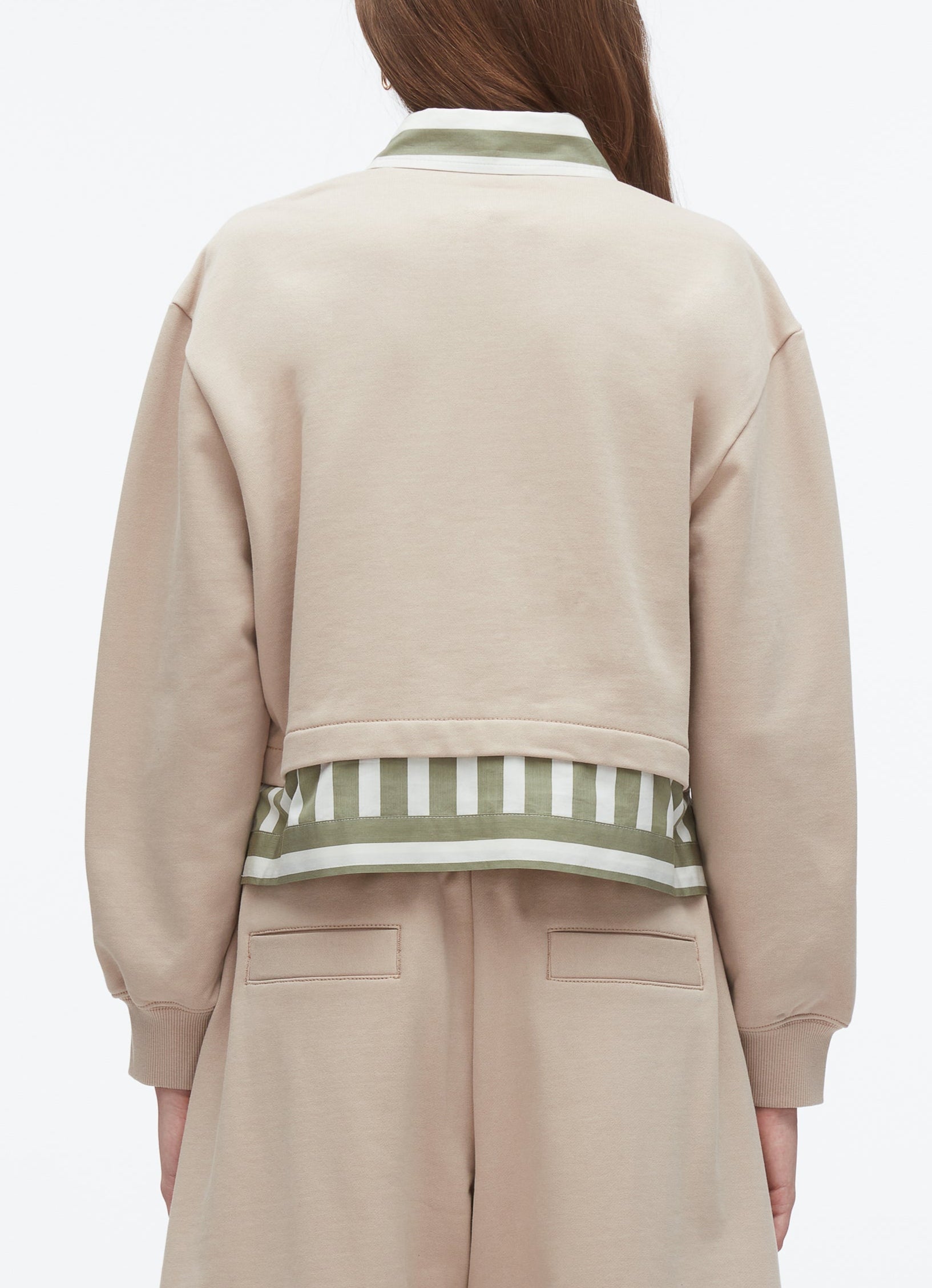 A person is seen from the back wearing the 3.1 Phillip Lim Cropped Polo with Stripe Combo Top, a beige jacket featuring green and white striped silk-cotton trim at the hem, paired with beige pants.