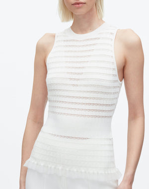 A woman wears the 3.1 Phillip Lim Shadow Stripe Tank, a sleeveless white fine-gauge knit top featuring semi-sheer horizontal textured stripes and a ruffled peplum hem.