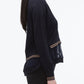 A woman stands in profile against a white background, wearing the 3.1 Phillip Lim Chiffon Hem Boxy Cardigan with striped cuffs and layered hem, paired with dark pants.