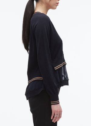 A woman stands in profile against a white background, wearing the 3.1 Phillip Lim Chiffon Hem Boxy Cardigan with striped cuffs and layered hem, paired with dark pants.