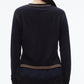 A person with dark hair in a low ponytail is shown from the back, wearing the 3.1 Phillip Lim Chiffon Hem Boxy Cardigan in navy with beige stripes at the hem and cuffs, paired with black pants.