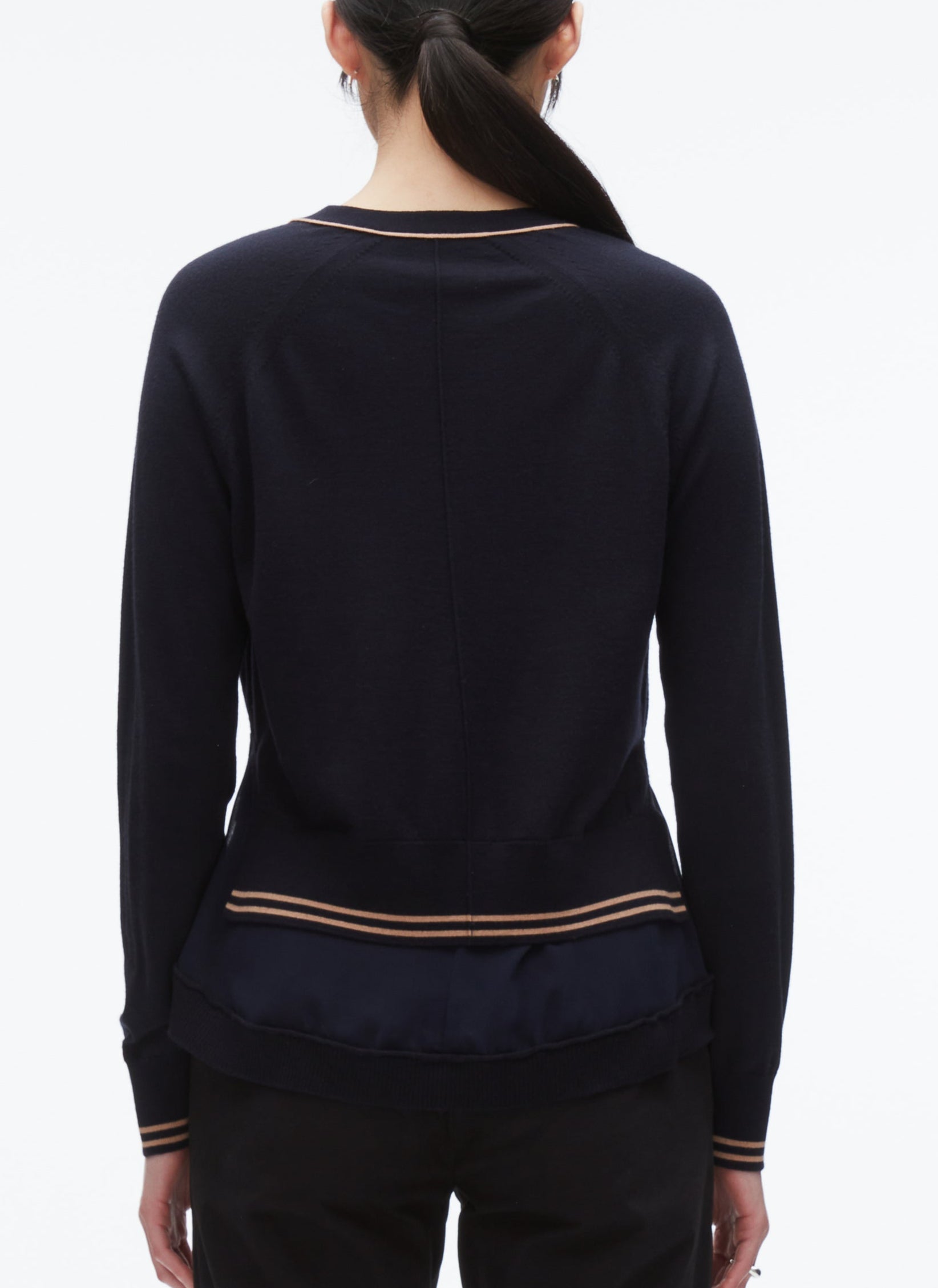 A person with dark hair in a low ponytail is shown from the back, wearing the 3.1 Phillip Lim Chiffon Hem Boxy Cardigan in navy with beige stripes at the hem and cuffs, paired with black pants.