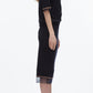 A woman stands in profile wearing the 3.1 Phillip Lim French Tuck Knit Dress with Organza, a black body-skimming silhouette featuring sheer trim, paired with black heeled sandals.
