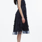 A woman in profile wears the 3.1 Phillip Lim Fil Coupé Midi Dress—navy blue, sleeveless cotton voile with embroidered floral accents—paired with navy flats and a ponytail, posing against a white background.