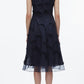 A woman faces away, wearing the 3.1 Phillip Lim Fil Coupé Midi Dress in navy cotton voile with a sheer upper back and embroidered florals, paired with flat sandals.